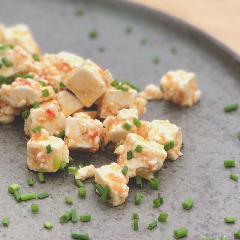 Das Bild zeigt eingelegten Feta  mit Käseheld von der Chilli Manufaktur und Schnittlauchröllchen auf einem Teller